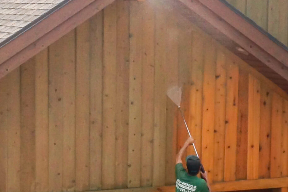 Wood restoration professional pressure washing wood siding over a garage.