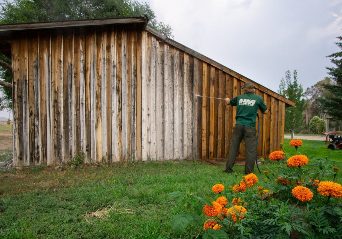 Example of our services. Nu-Wood 2 empoyee spraying the side of a barn. You can see what old wood and new wood looks like.