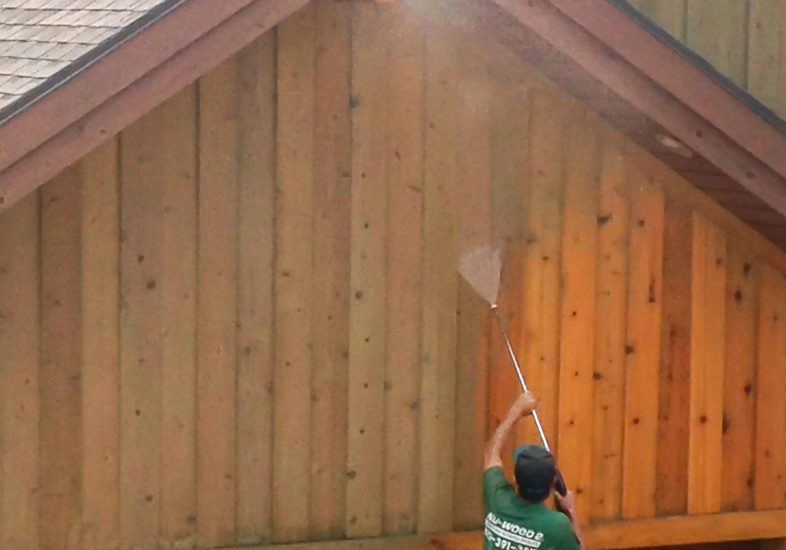 Wood restoration professional pressure washing wood siding over a garage.